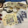 Diverse mynt, sedlar, armbandsur, fickknivar och munspel.